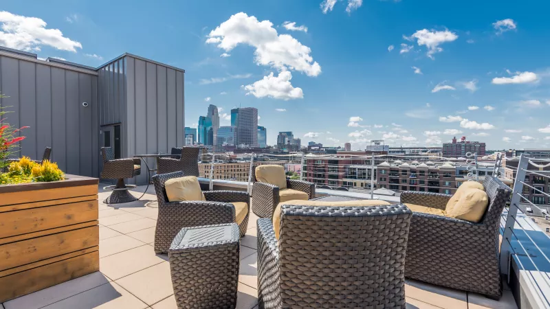 Rooftop patio with wicker furniture, yellow cushions, city skyline, and blue sky.