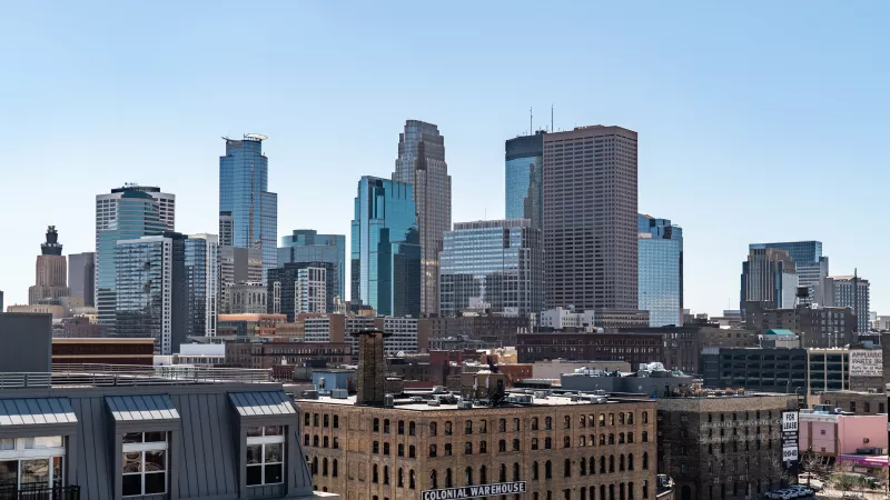 Daytime city skyline with a mix of modern glass skyscrapers and older brick buildings under a clear blue sky. Photograph.